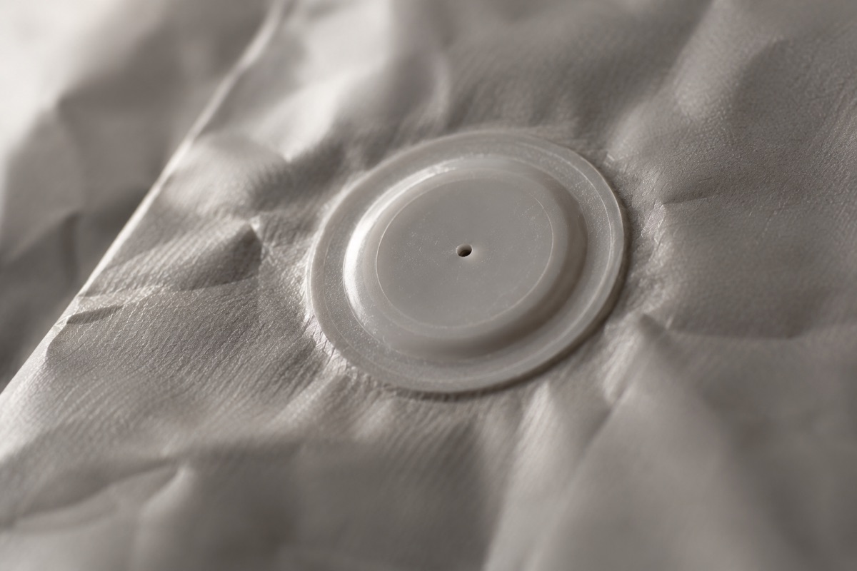Macro view of a round plastic one-way valve with a small central vent on a grey coffee bag