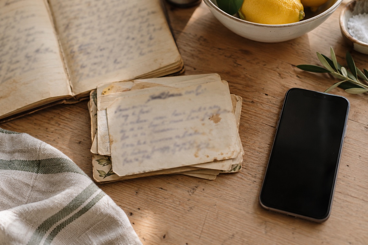 Old handwritten recipe cards and a notebook on a wooden table next to a smartphone